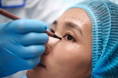 Closeup image of young woman getting face marked before blepharoplasty clipart
