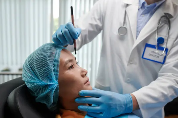 Cropped image of plastic surgeon marking face of young woman before surgery