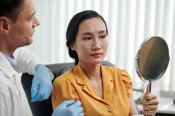 Vietnamese woman looking at mirror enjoying her new nose after surgery