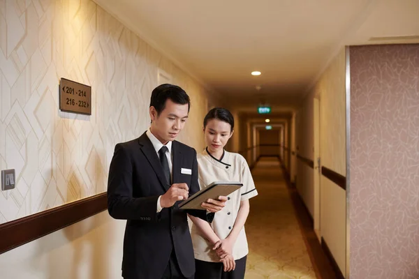 Manager and hotel maid checking list of guests on tablet computer before cleaning rooms