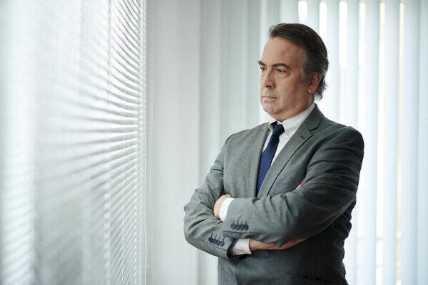 Portrait of mature businessman in grey suit crossing arms and looking away