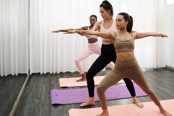 Yoga coach correcting young woman doing warrior pose in class