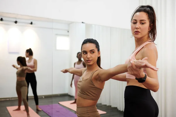 Yoga teacher showing client how to spread arms when doing warrior pose
