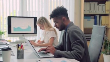 Bilgisayarda çalışan çeşitli girişimcilerin orta ölçekli bir görüntüsü. Ofisin yanındaki masada oturup mali tabloları izliyorlar.
