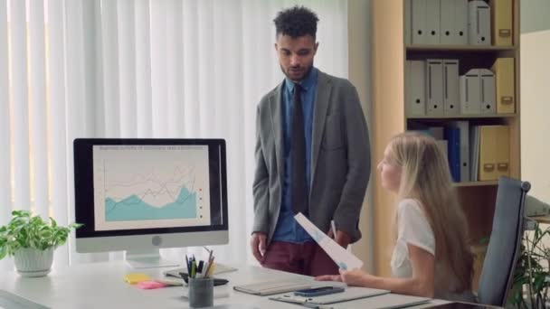 男性经济学家与同事讨论公司的增长指标 同时站在办公室电脑屏幕上的图表旁边 — 图库视频影像