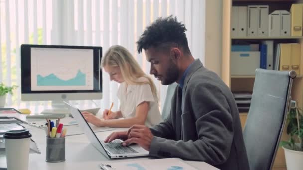 不同企业家在笔记本电脑上工作的中景照片 他们坐在旁边的办公桌前 用财务图表进行监控 — 图库视频影像