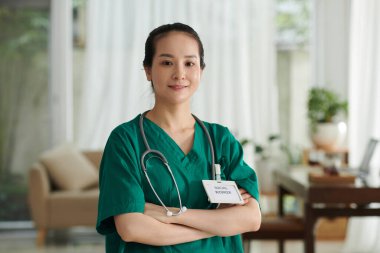 Hasta dairesinde duran üniformalı, gülümseyen Vietnamlı sosyal görevli portresi.