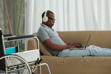 Engelli koltuğunun yanındaki tekerlekli sandalye koltukta otururken dizüstü bilgisayarla çalışıyor.
