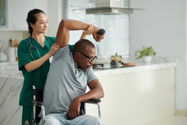 Fizyoterapist hastadan elinde dambılla yan eğilmesini istiyor.