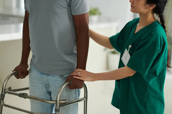 Cropped image of social worker supporting patient making steps with walkers