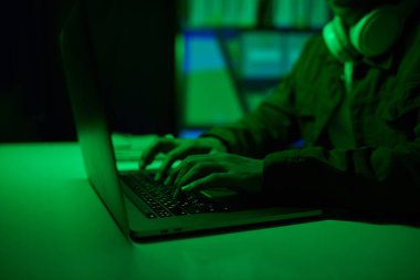 Hacker, neon yeşil ofis odasında dizüstü bilgisayarla çalışıyor.
