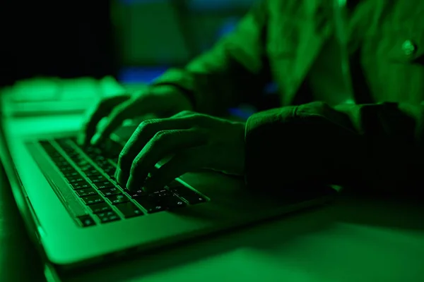 Closeup image of developer coding on laptop in green neon light
