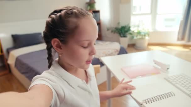 彼女のチューターとのビデオ通話中に話している小さな女の子のPovショットと子供部屋に立っているカメラにノートブックを示す — ストック動画