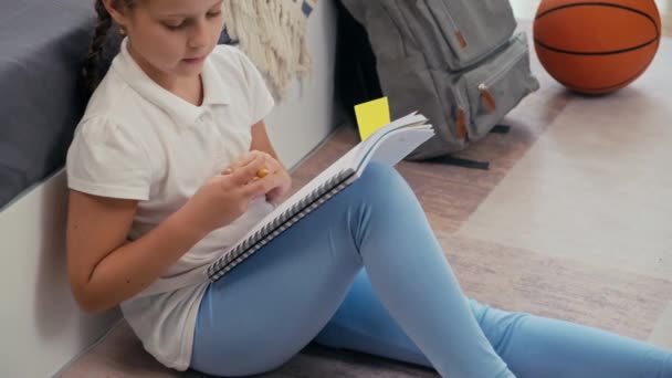 学校の後に彼女の部屋の床に座っている間 彼女の宿題のページにステッカーを置く14歳のコーカサス女の子のクロップショット — ストック動画