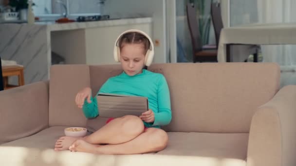 在数码平板电脑上观看社交网络视频的未成年少女的中长镜头 而睡在带小吃的沙发上 — 图库视频影像