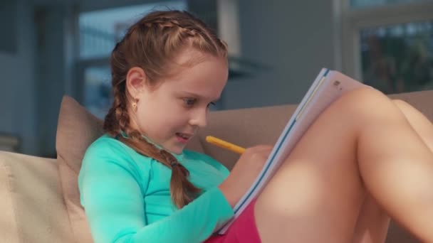 女性の子供は 宿題をしながらワークブックで何かを書く 屋内ソファーで休む — ストック動画