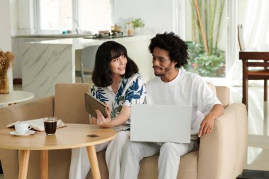 Tabletli genç bir kadın kocasına online ürünleri ekranda gösterirken aynı zamanda satın almak ve fiyat konusunda ona danışmak için bir şey seçiyor.