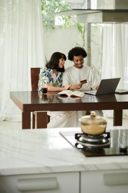 Mutlu genç adam kredi kartına bakıyor ve internet sayfasına numarasını giriyor. Evde eşiyle birlikte online eşyalar sipariş ediyor.