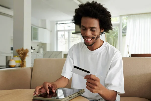Boldog Fiatal Afro Amerikai Férfi Néz Hitelkártya Kezében Miközben Kanapén — Stock Fotó
