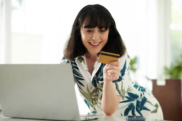 Young smiling woman with credit card bending over laptop during e-shopping and contactless payment for purchase in online shop