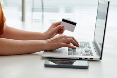 Bilgisayardaki klavye üzerinden alışveriş yapan genç bayanların yan görüntüsü. Bir kısmını seçerken bir yandan da online mağazada eşyalar arasında geziniyorlar.