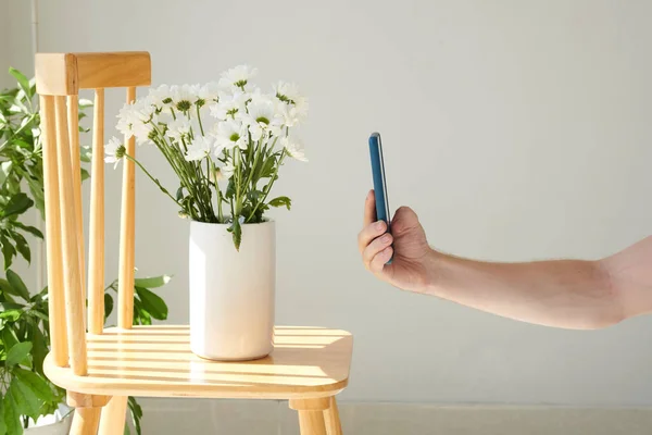 Man taking picture of vase with flowers on smartphone to post on social media