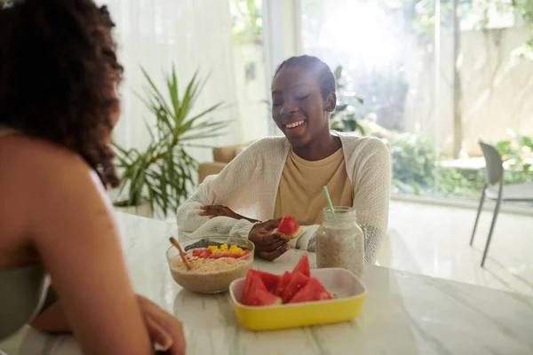 Smiling Black young woman eating breakfast in kitchen of her friend