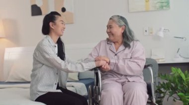 Tekerlekli sandalyedeki son sınıf öğrencisi genç kızıyla bakımevinin yatak odasında konuşurken orta boy bir fotoğraf.