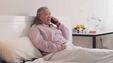 Hasta, olgun bir kadının yatakta dinlenirken kocasını cep telefonundan araması.