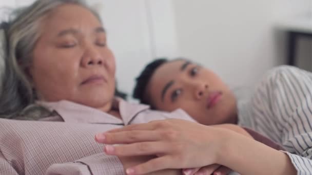 年轻而悲伤的亚洲女儿躺在卧床卧床的年老母亲胸前 注意力不集中 — 图库视频影像