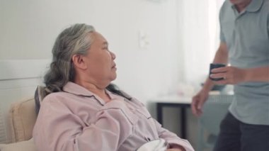 Yaşlı kocasının hasta karısına evde bakıcılık yaparken ona sıcak çay verirken orta boy bir fotoğrafı.