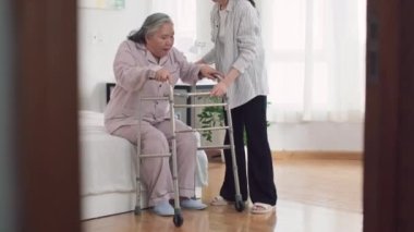 Genç Asyalı bakıcının, yaşlı kadın hastaya Walker 'la hastanede ayağa kalkması için yardım ederken orta boy fotoğrafı.
