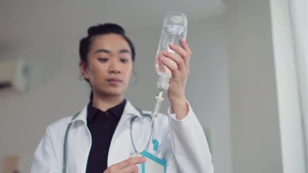 病気の患者のためのドロップカウンターを設定する若いアジアの女性医師のチルトダウンショット — ストック動画