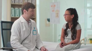 Klinikte yıllık check-up sırasında Asyalı genç kızı neşelendirirken orta boy bir erkek doktor fotoğrafı.