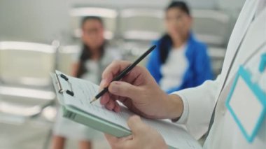 Klinikte bekleyen iki kişilik ailesi olan hasta bir hastanın tıbbi kartını dolduran doktorların seçici elleri.