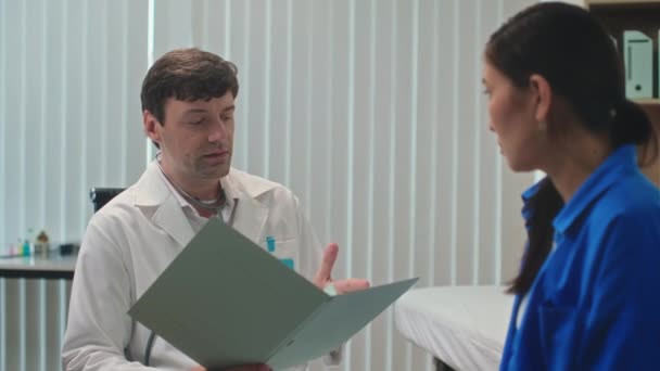 女性患者の医療カードを見て 診療所で診察中に診断を説明する医師 — ストック動画