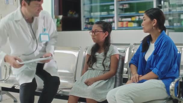 任命中に病院のホールで母親の隣に座っている10代の少女に挨拶する白いコートの医療従事者の中型ショット — ストック動画