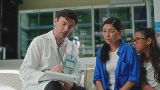 진료소의 구역에 앉아있는 아이와 환자에게 서류에 서명하도록 요청하는 코트의 의사의 — 비디오