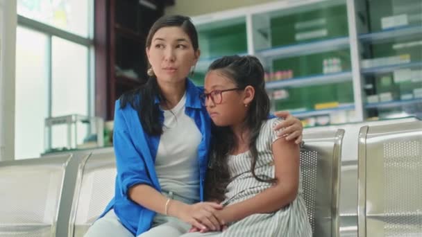 ロビーで医者を待っている間彼女の恐ろしい十代の娘を抱擁する母親の中長いショット — ストック動画