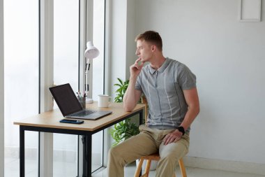 Düşünceli yazılım geliştiricisi ofisindeki ofis masasında oturup pencereden bakıyor.