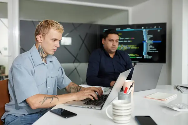 Serious software developer coding on laptop at office desk