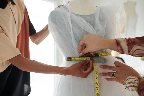 Hands of tailor measuring mannequin with wedding dress