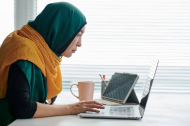 Erişkin Müslüman iş kadını tesettüre girmiş, bilgisayardan e-posta okuyor.