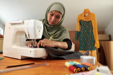 Müslüman moda tasarımcısı müşterisi için elbise dikiyor