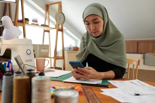 Muslim fashion designer in hijab reading text messages from clients