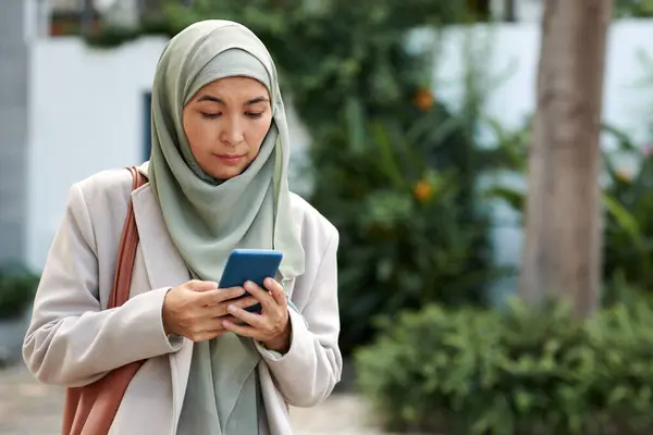 Muslim woman in hijab reading text messages on smartphone