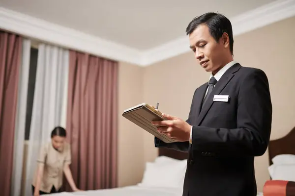 Spa resort manager signing document on tablet computer when maid making bed