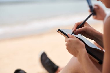 Plajda otururken tablet bilgisayarında resim çizen kadının yakın plan resmi