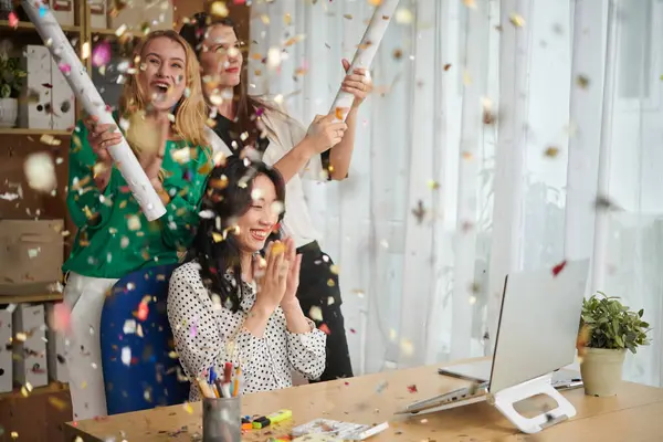 Business colleagues exploding party poppers with sparkling confetti to celebrate finishing of big project