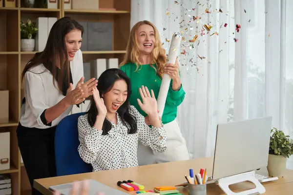 Joyful businesswomen exploding party poppers celebrating success of online product presentation